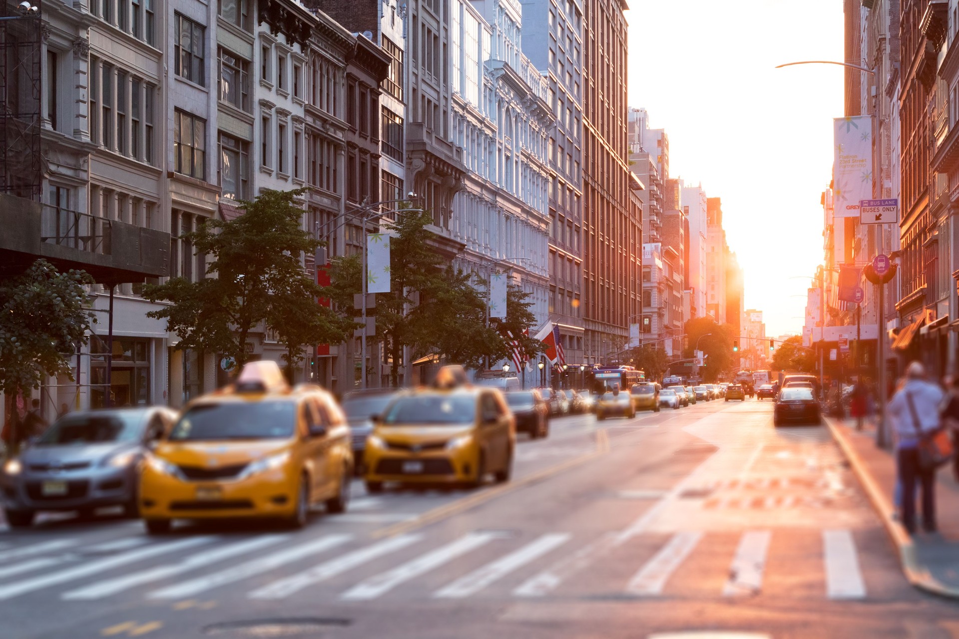 Sunlight shines down the streets of New York City with taxis stopped at the intersection